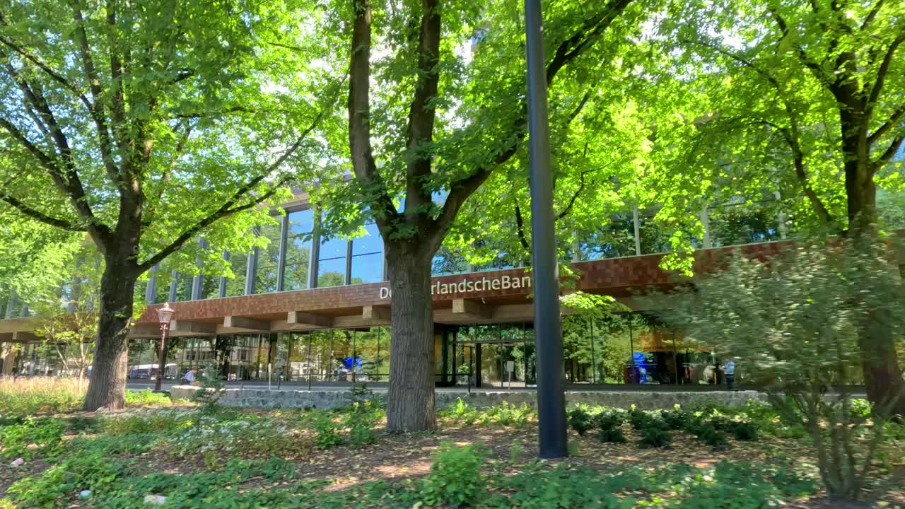 Contemporary financial institution with glass facade, surrounded by trees, captured in smooth lateral camera movement