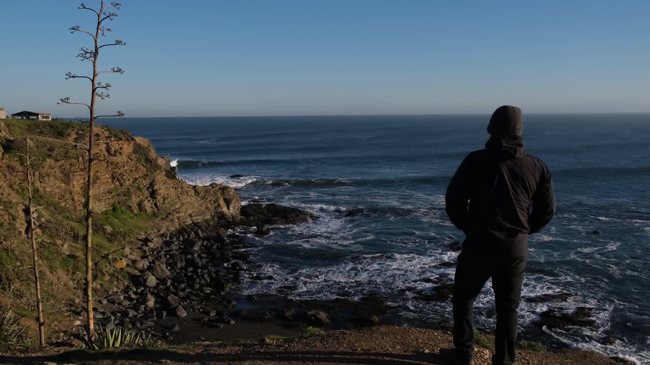 traveler man looking at the sea in pichilemu punta de lobos chile with the sun in a sunrise watching people surf and landscape lookout's waves chilean