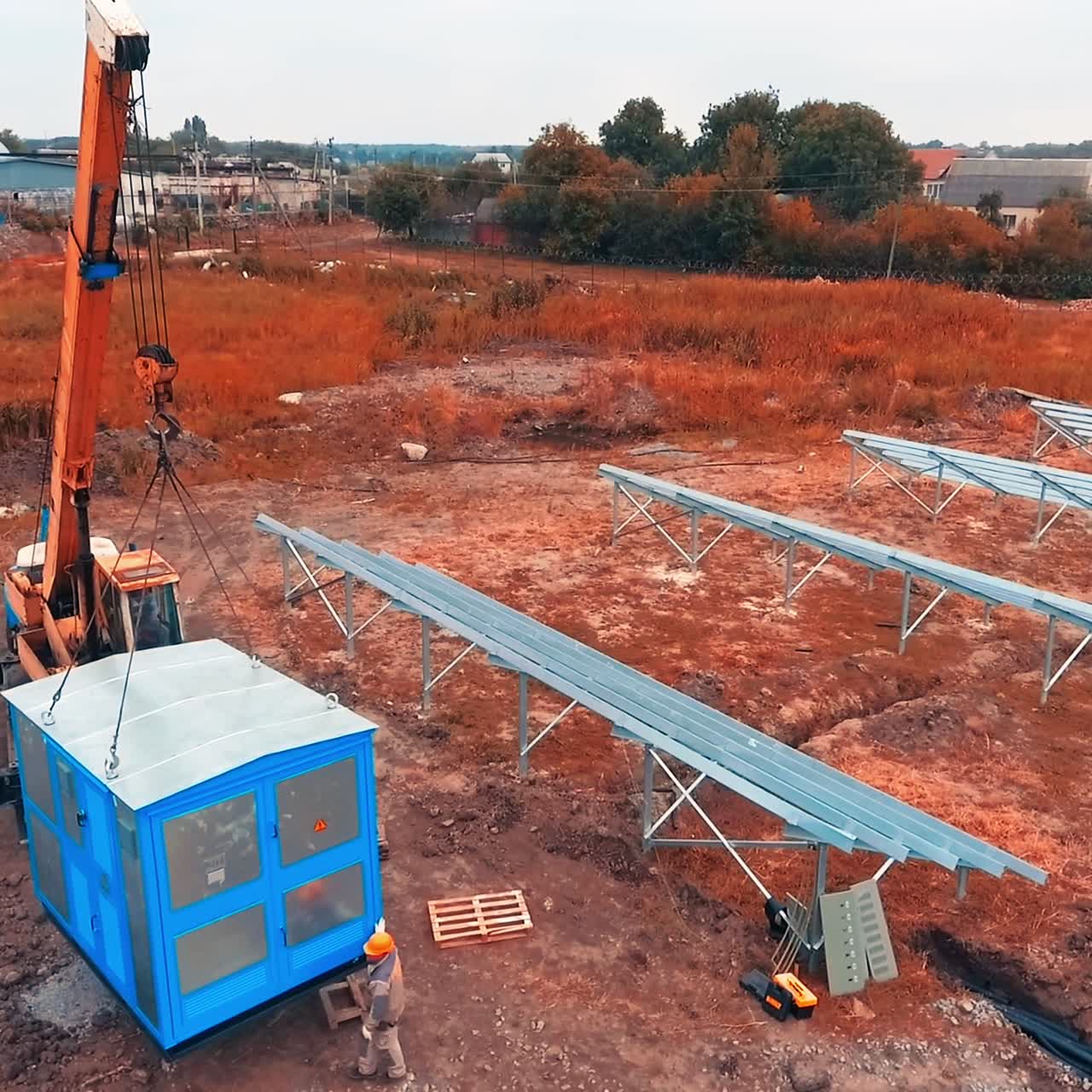 Metal booth being lifted and transported by the crane. Male worker controlling the process. Construction site backdrop