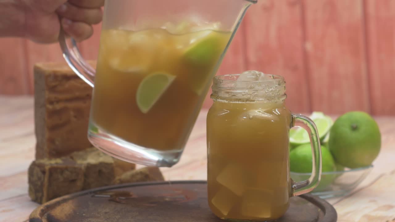 Refreshing lemon drink to beat the hot weather.close-up shot capturing hands placing a glass mug with ice on a wooden table, and serving from a pitcher of a traditional Latin American beverage
