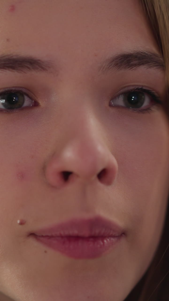 Face of pretty young woman with mole near upper lip looks hopefully into camera on blurred background closeup. Portrait of attractive female model