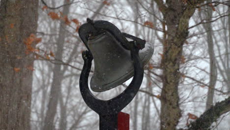 slow motion snowfall on snowy winter day with outdoor bell in background