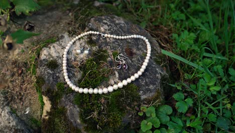 wedding earrings and pearl necklace for the bride laid on a stone in nature