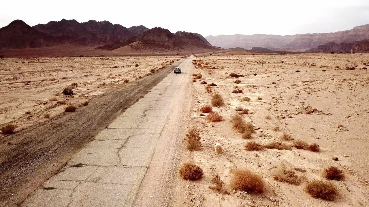 Passenger car drives left-handed fast away on the torn dry dirt road between the red canyon in the dry Timna Park in the Negev Desert in southern Israel on a sunny day
