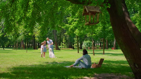 father training labrador with children in park. mother watching game with dog.