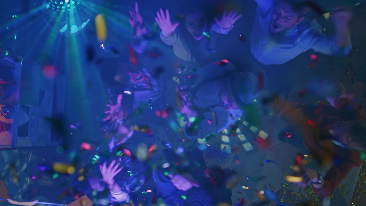 en la fiesta del club: un grupo diverso de amigos se divierten, bailan, socializan y beben. disparando con una pistola de confeti. jóvenes elegantes bailan enérgicamente en la sala de estar. disparo de arriba hacia abajo.