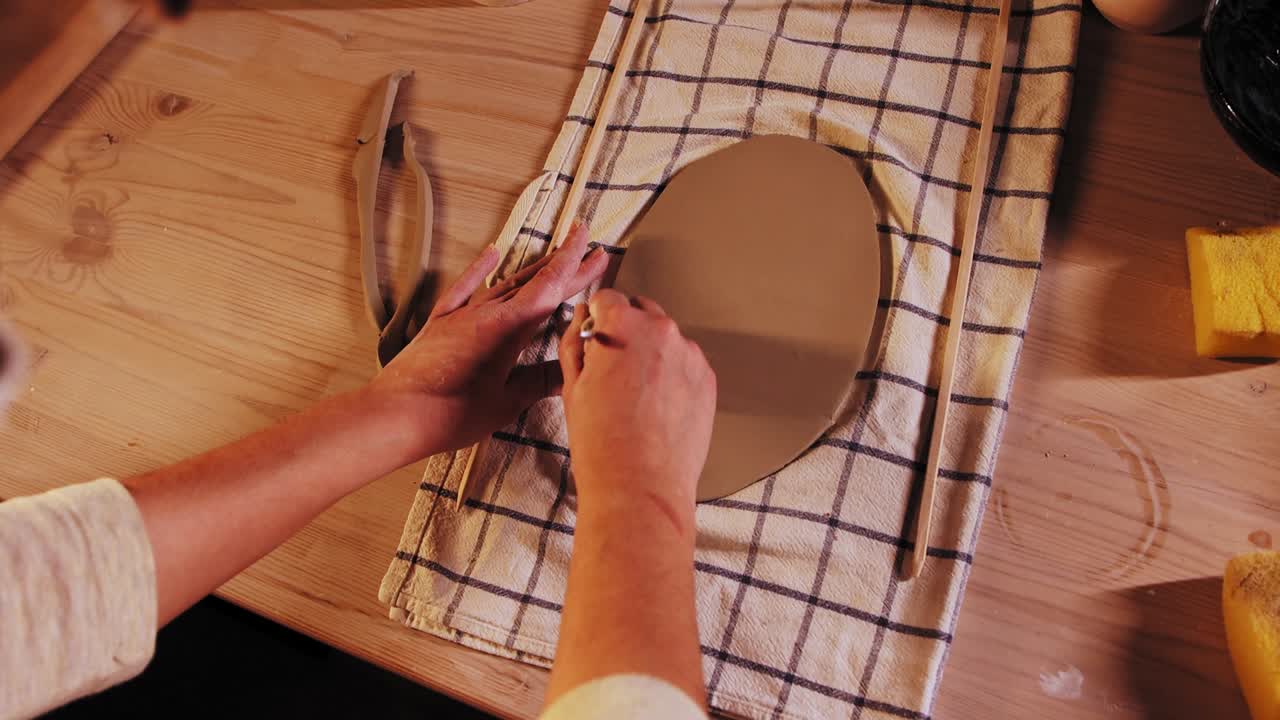 cerámica en el estudio - joven mujer alfarera cortando los bordes de un pedazo de arcilla en la mesa