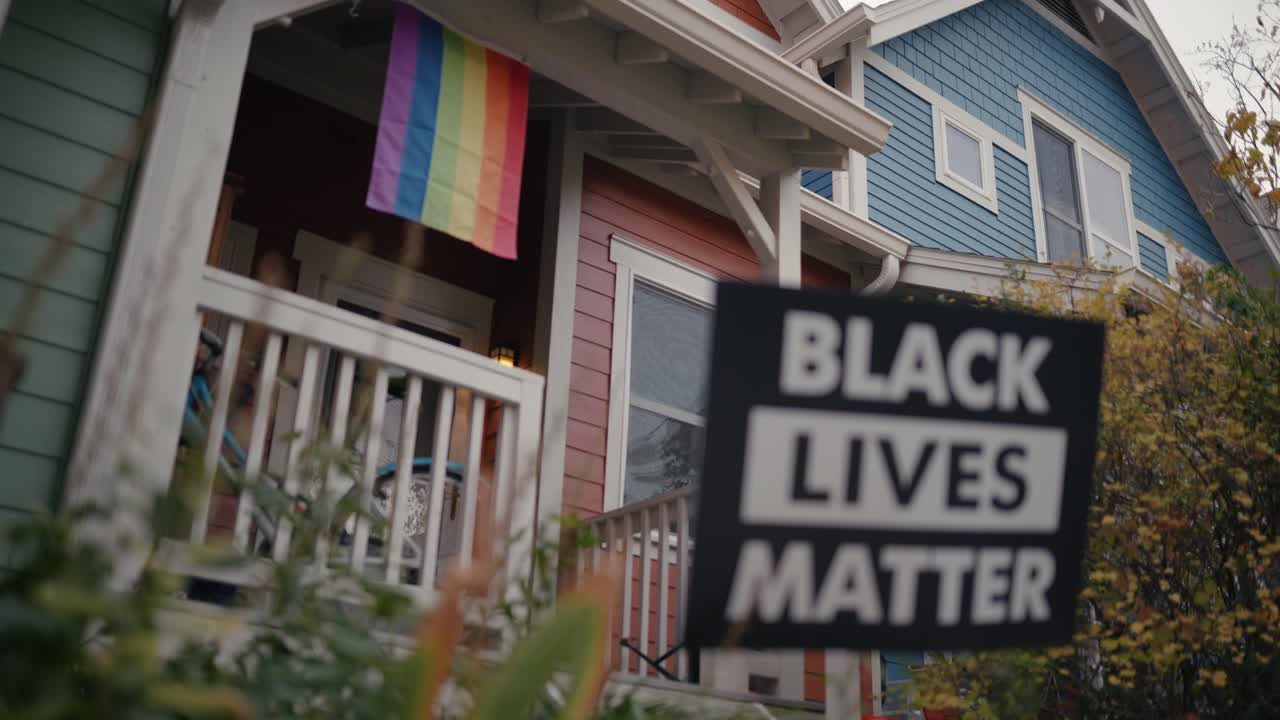 Black Lives Matter sign in colorful front yard with Pride Flag in the background.