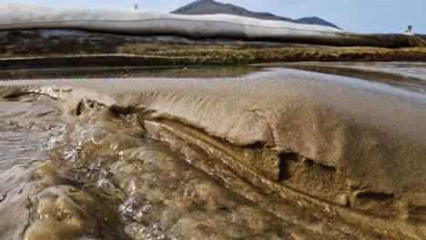 Powerful-water-stream-washing-out-beach-sand,-close-up-view