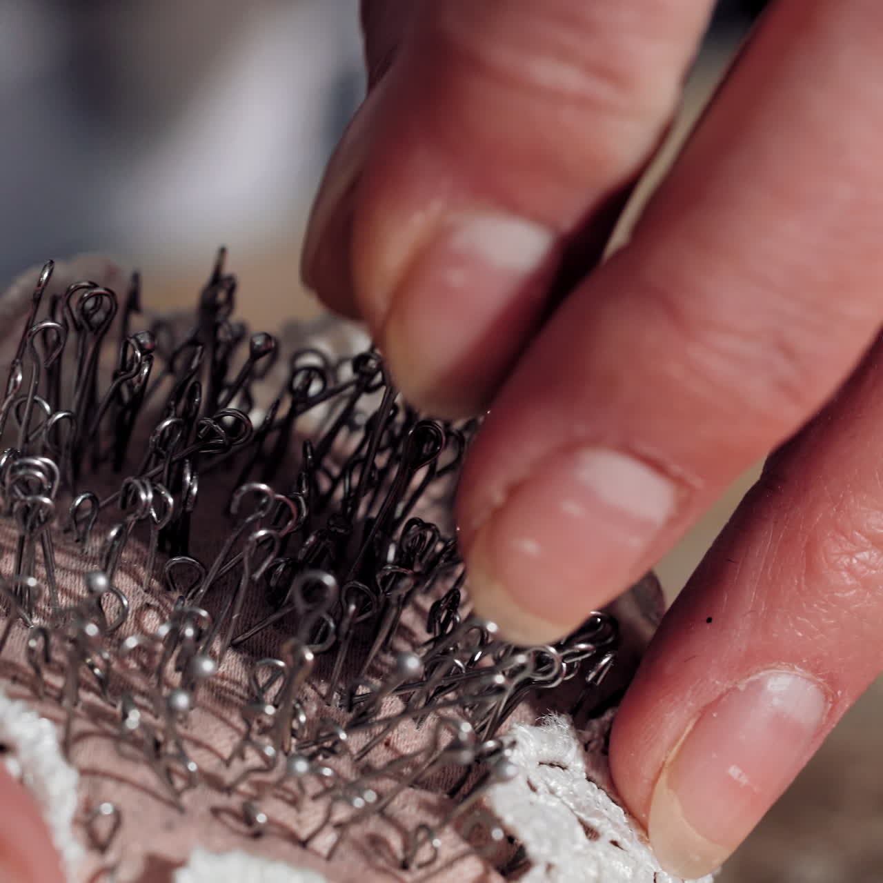 Hand of a seamstress is taking pin from workplace in atelier. Many black sewing pins in special pin pillow on a table. Close-up.