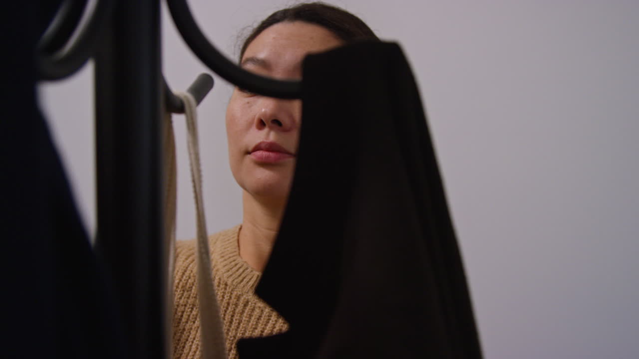 쇼핑에서 돌아오는 여성이 가방을 집으로 가져오기 전에 코트를 스탠드에 매달고 있습니다.