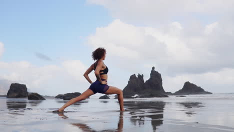 En-Cámara-Lenta,-Una-Mujer-Joven-Se-Encuentra-Junto-A-La-Orilla-Del-Océano,-Practica-Estiramientos-Y-Yoga-Mientras-Mira-A-Lo-Lejos,-Encarnando-La-Serenidad.