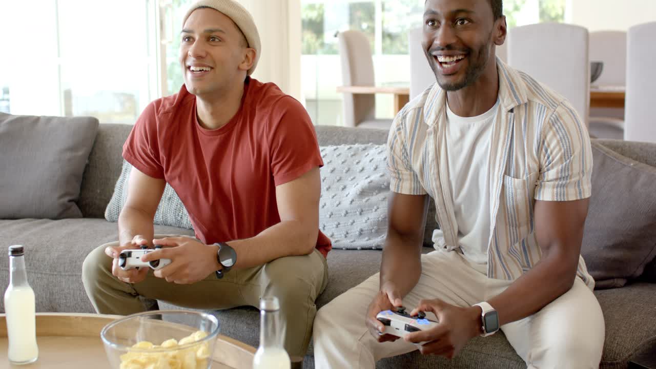 Diverse male friends grabbing controllers, launching game for fun and reacting at home with snacks