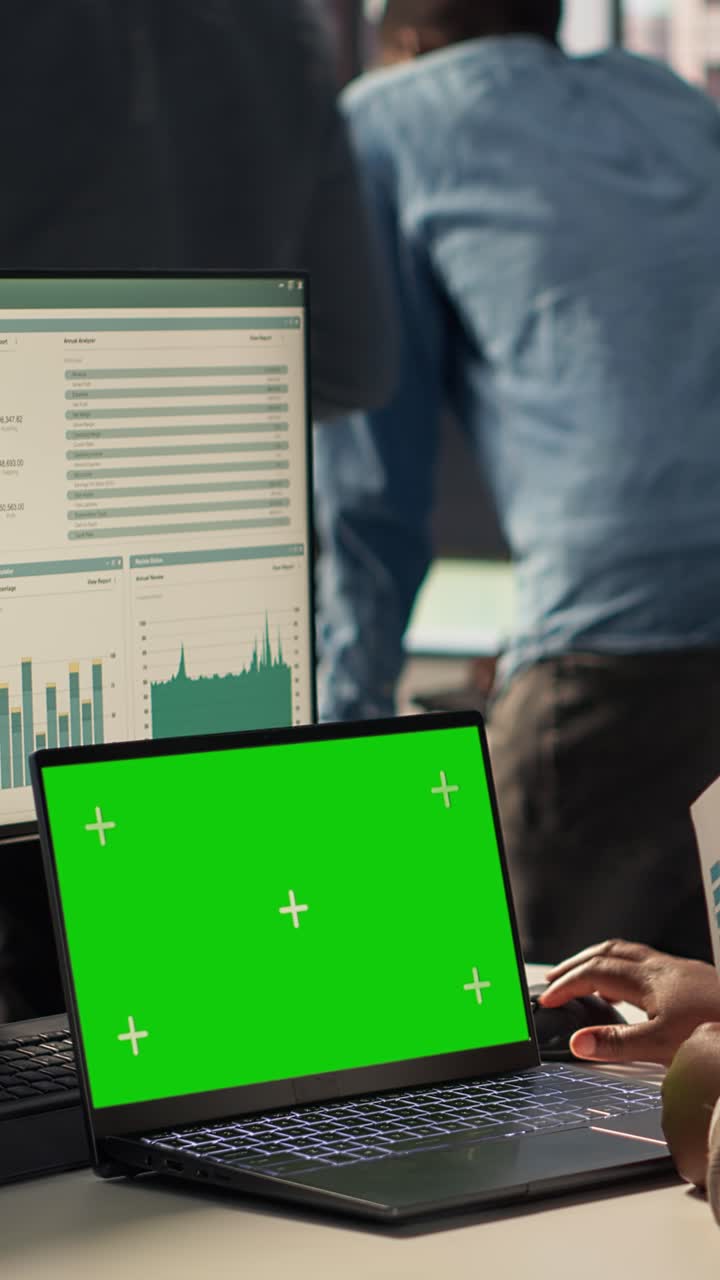 Person Working on Laptop with Green Screen Display in Office
