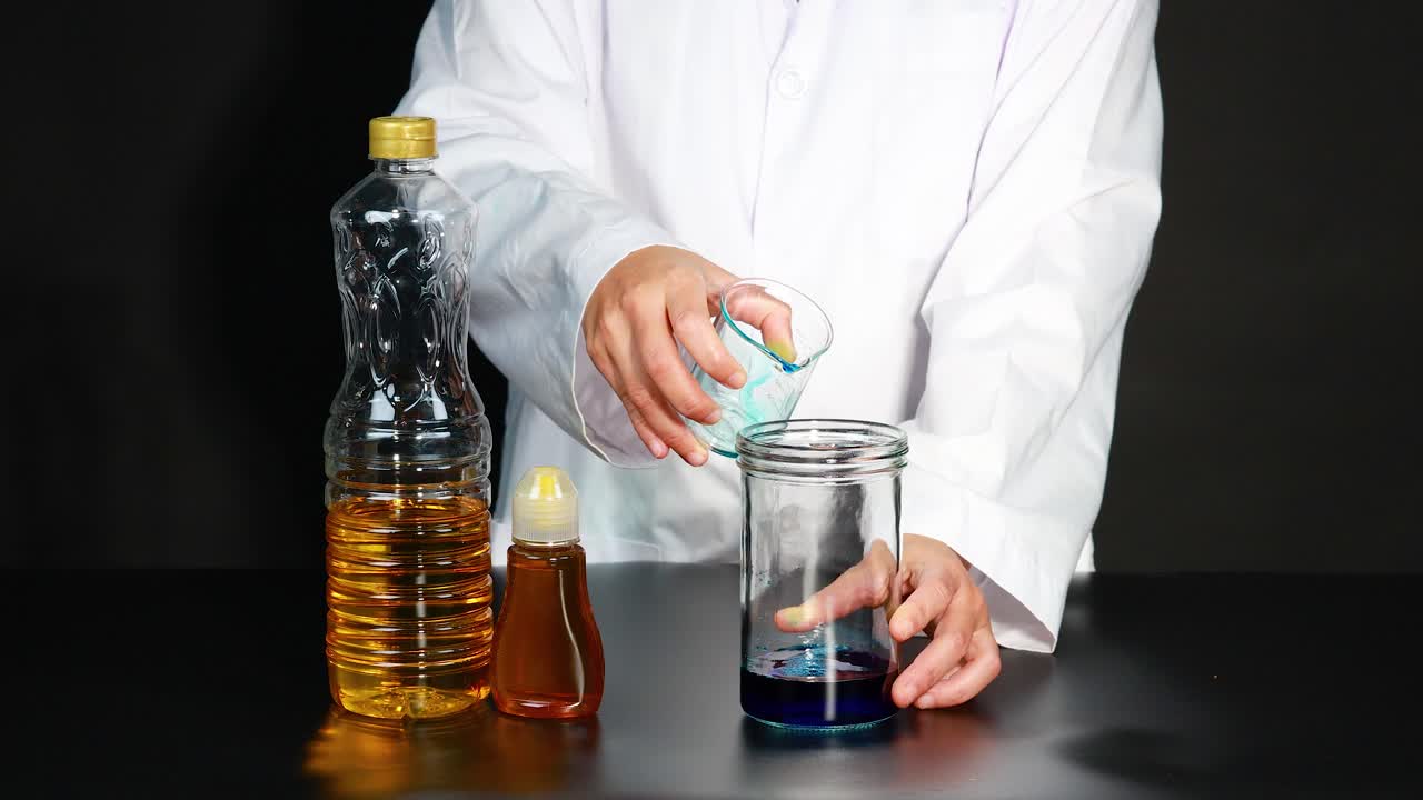 una persona con una bata de laboratorio vierte líquido azul en un frasco, rodeado de botellas, demostrando un experimento científico