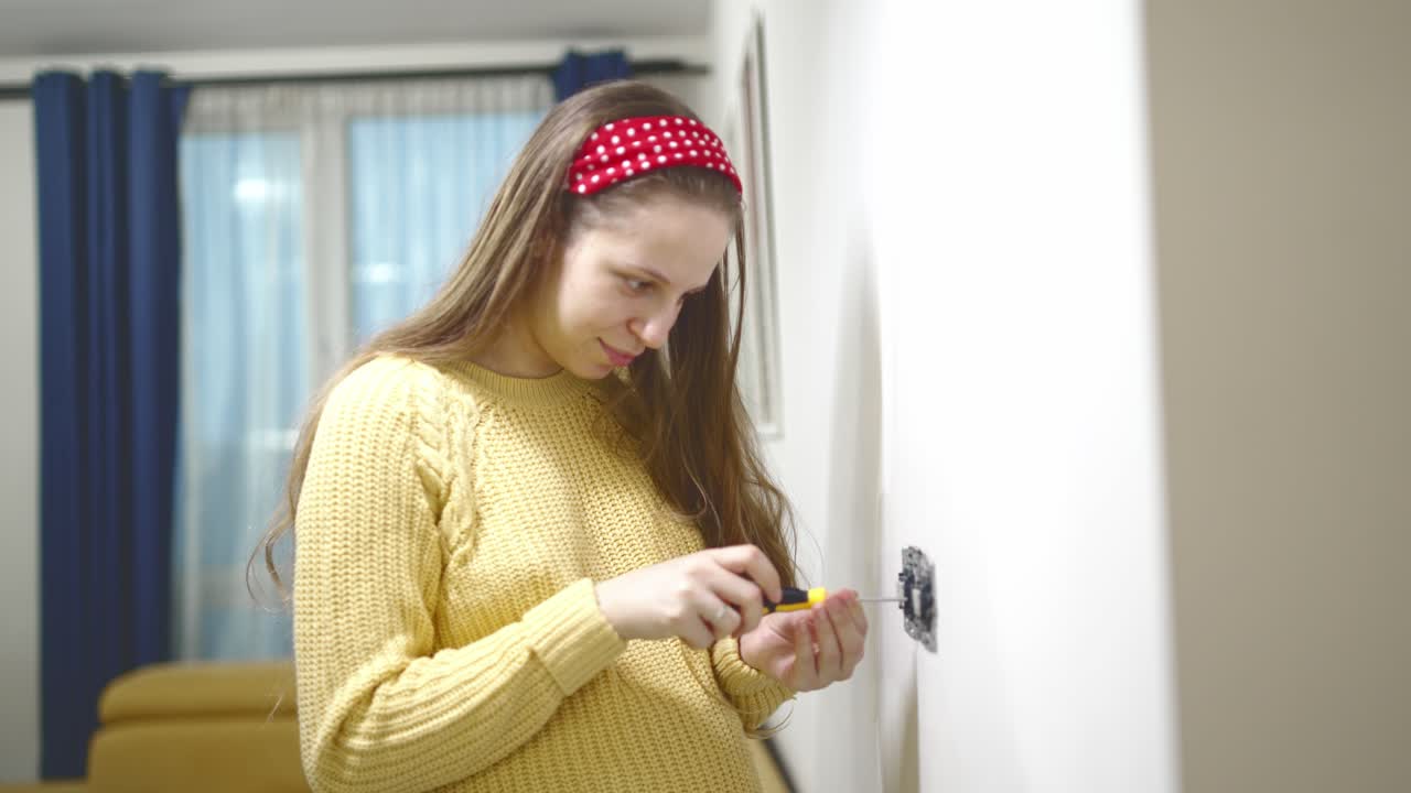 Woman at home repairing electrical outlet with screwdriver as part of DIY project. Hands-on home improvement, electrical safety, personal maintenance, indoor repair, practical household task