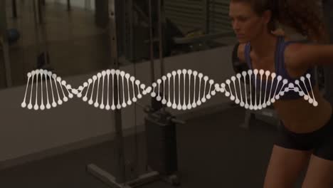 Animation-of-dna-strand-over-strong-woman-exercising-in-gym