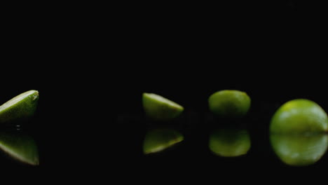 several green ripe limes fall on the glass with splashes of water in slow motion on a dark background