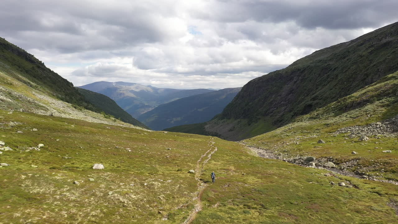 Escursionista che scende una bellissima valle verde tra le montagne in Norvegia