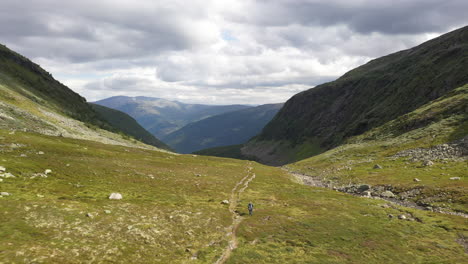 person hiking down a beautiful green valley in the mountains in norway