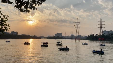 tourists pedal boating for amusement at lake in city park at sunset, wide shot