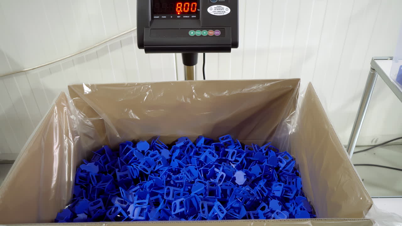 장갑을 입은 남자가 공장에서 스케일의 큰 상자에 파란 플라스틱 클립을 던집니다.