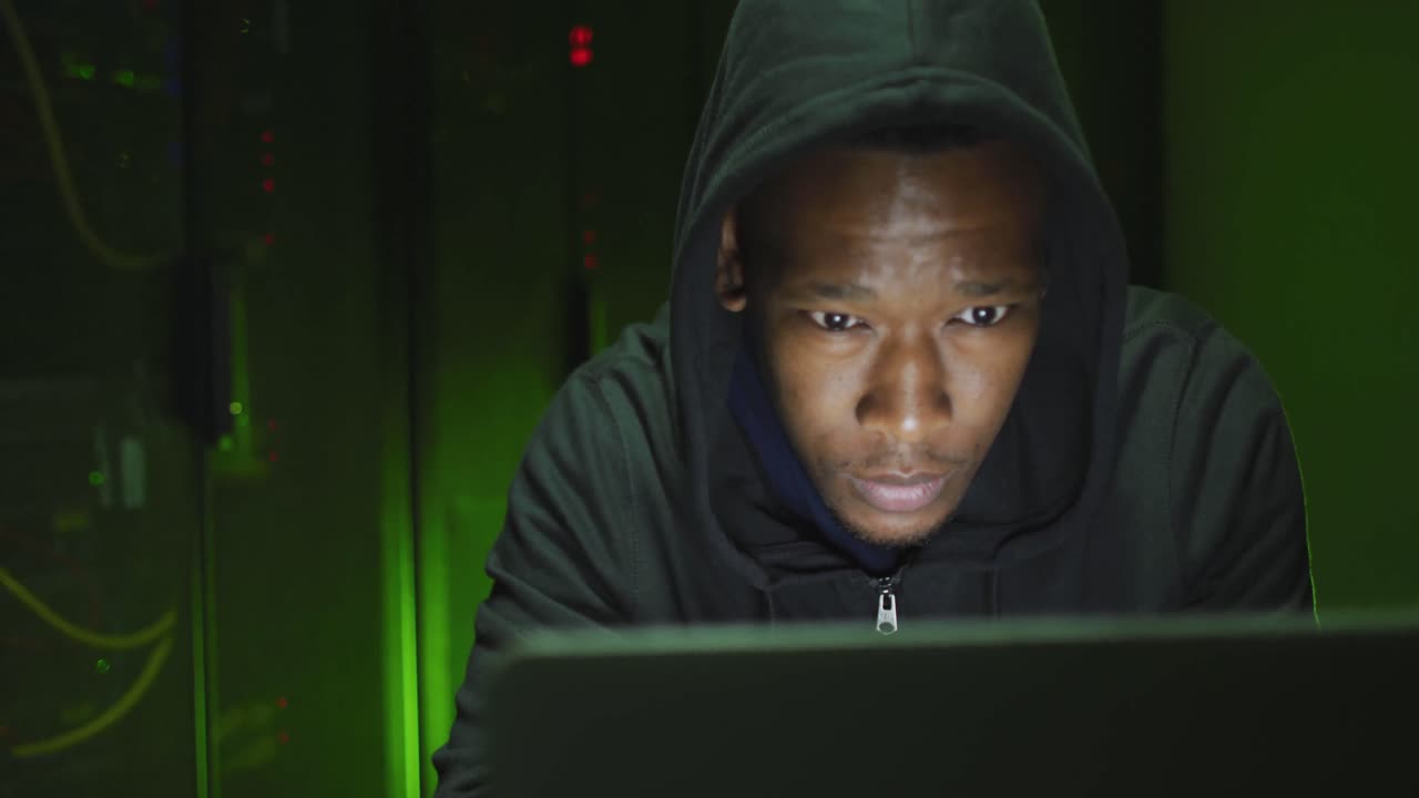 Hacker informatico uomo afroamericano che usa un laptop in una sala server aziendale