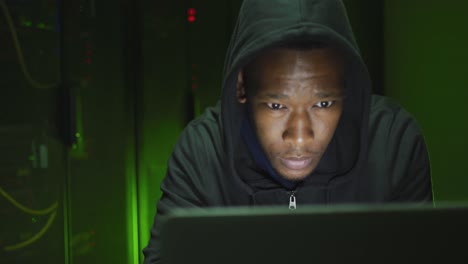 African-american-male-computer-hacker-using-laptop-in-business-server-room