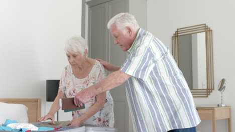 una pareja caucásica senior haciendo las maletas en el dormitorio de su casa, en cámara lenta.
