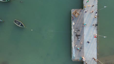 fisherman throws out fishing net in the sea from pier, aerial top down