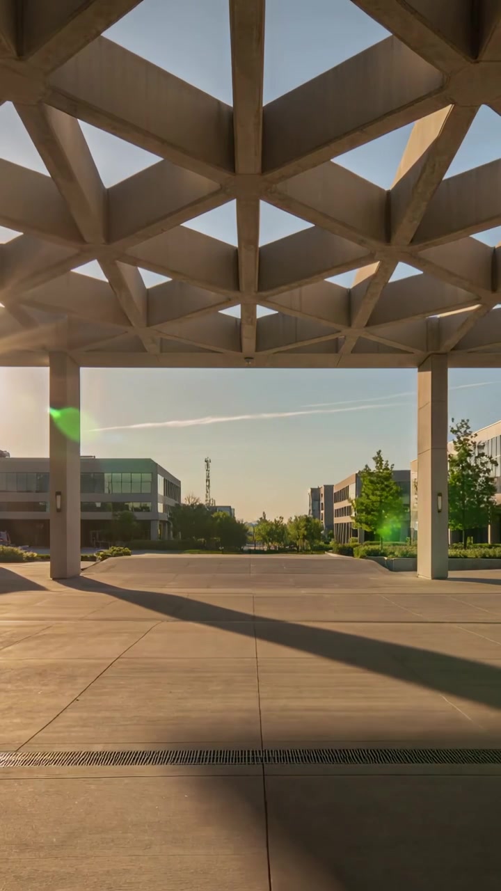 Vídeo vertical: Marquise enquadrada com duas colunas projetando longas sombras no campus, reflexo de lente do sol baixo.