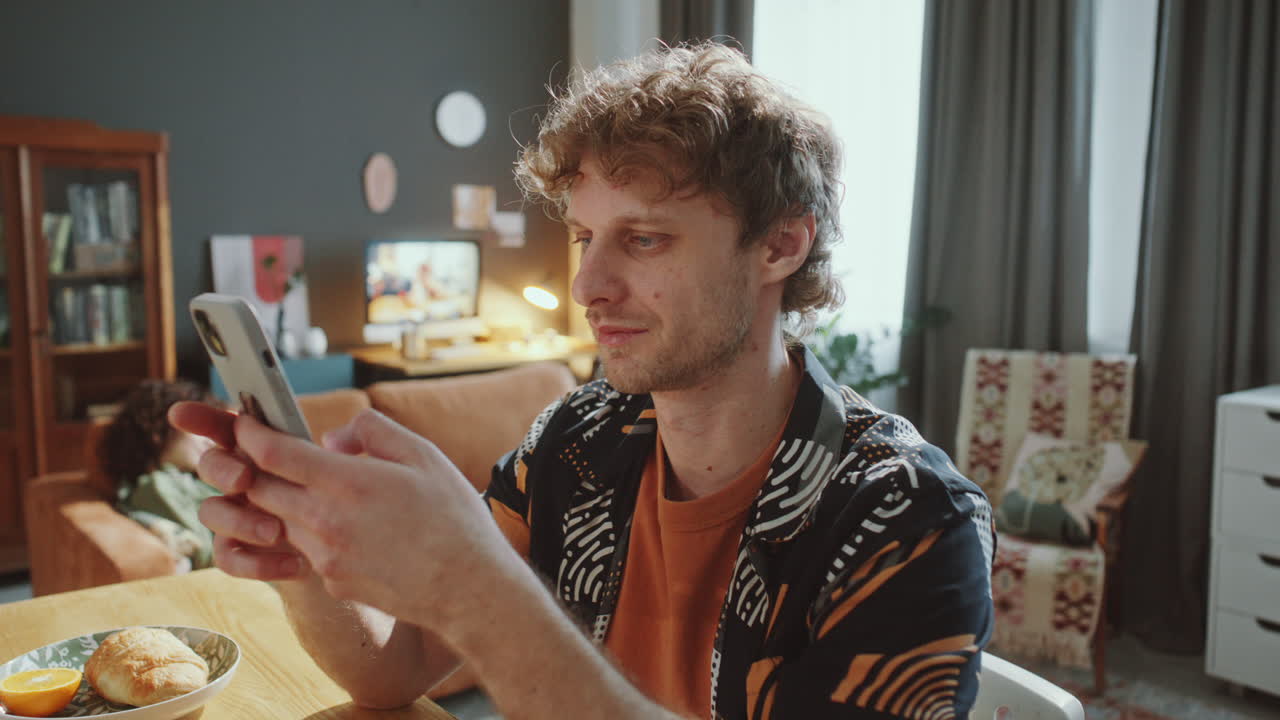 Smiling Man Browsing Smartphone at Kitchen Table during Day at Home