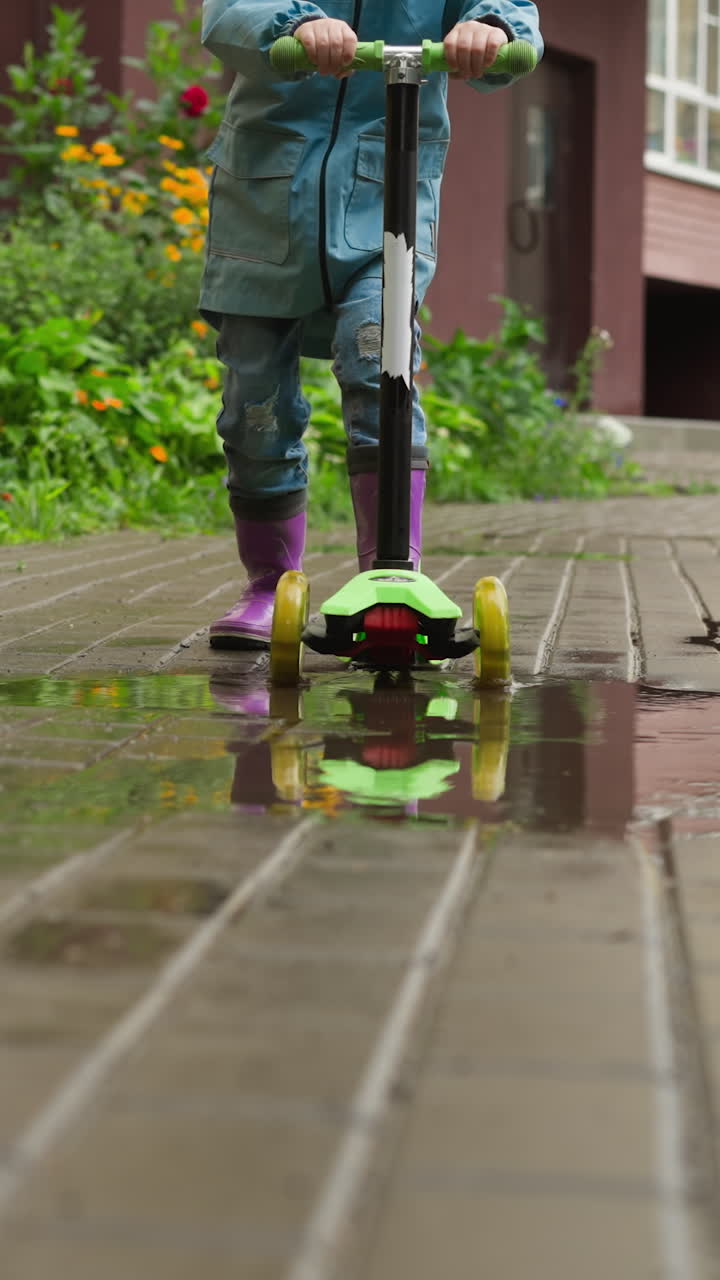 Bambino scivola sullo scooter con tempo piovoso. Un bambino avventuroso si spinge in avanti sullo scooter a spinta, assaporando la libertà di movimento, non scoraggiato dal tempo piovoso.
