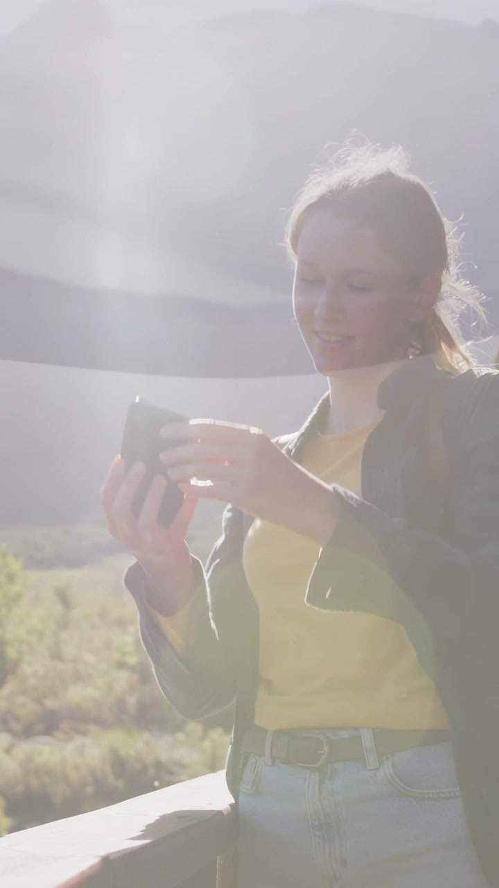 Video verticale: Donna che alza il telefono verso il sole creando un bagliore dell'obiettivo (lens flare) sopra una ringhiera e controlla le informazioni di viaggio.