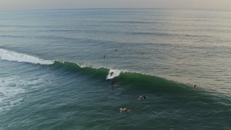 antena: surfista atrapando una gran ola rompiendo con otros surfistas remando al lado