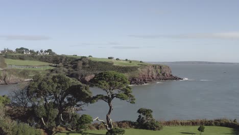 Aerial-rises-from-beautiful-green-Dunmore-East-Park,-sea-cliffs-beyond
