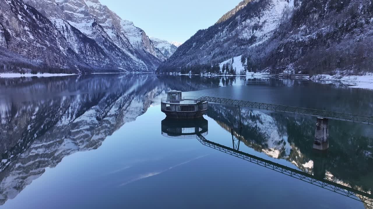 Aerial water intake tower reflecting on Klöntalersee in Klöntal, Switzerland, winter scene