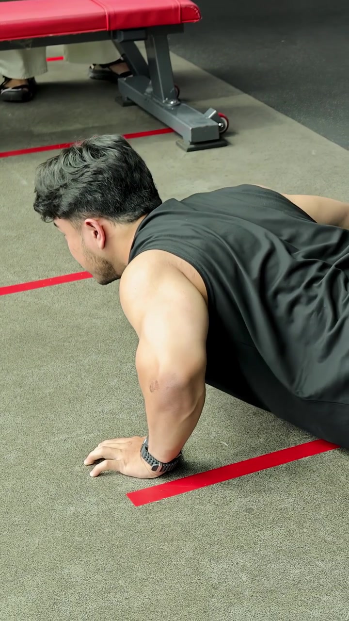 Side view of an athletic man performing push-ups on a gym floor with red markings.