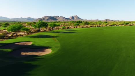 sweeping drone shot over a wide desert golf fairway with bunkers and distant mountain peaks in view