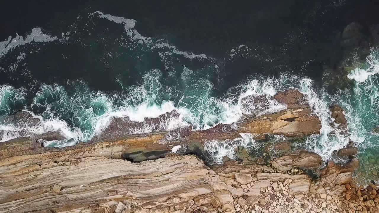Aerial view of ocean waves crashing against rugged rocky cliffs, showcasing the powerful forces of nature in Baleal, Portugal, with white foam swirling in the surf, , top down overhead drone shot