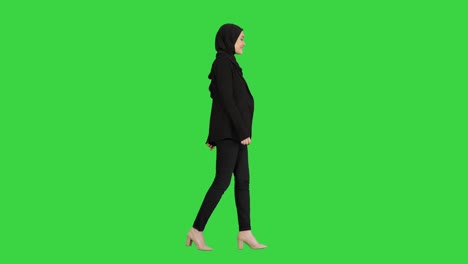 smiling islamic female model wearing hijab walking and looking ahead on a green screen, chroma key