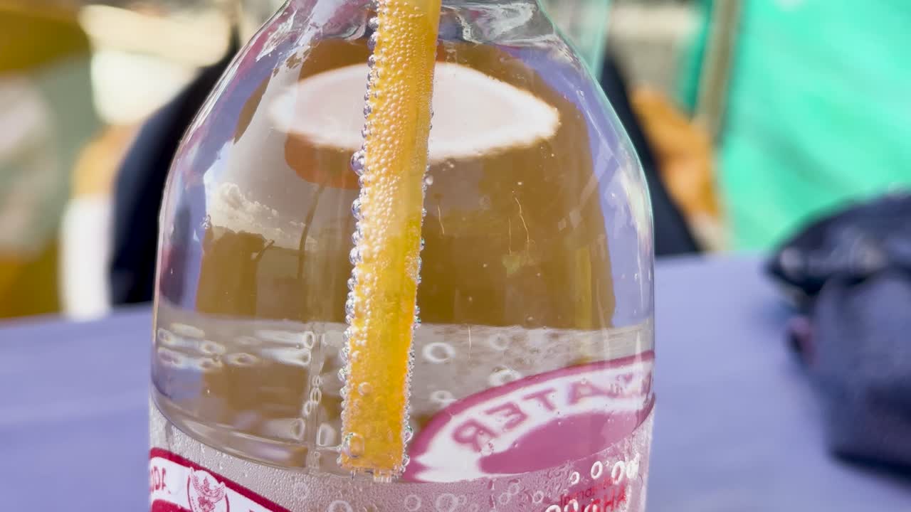 Close-up of bubbles forming around a straw in a soda bottle, showcasing cavitation phenomena in a bright setting