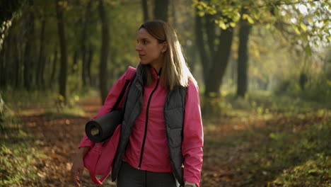woman walking through autumn forest with yoga mat
