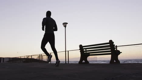 Animation-of-red-and-white-paint-brushstrokes-over-african-american-male-athlete-running-by-sea