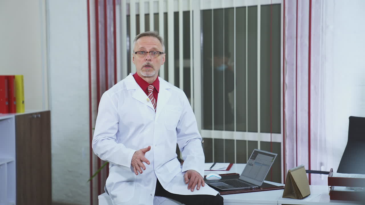 Dokter konferensi online melihat ke kamera. Tampilan depan dokter berbicara ke kamera di klinik