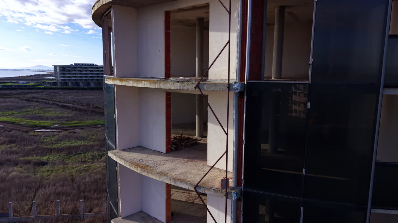 Desciende por el edificio inacabado con vanos vacíos. Hay algunos escombros dentro de la construcción.