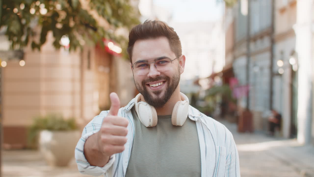 un joven caucásico alegre que muestra dos pulgares hacia arriba da una respuesta positiva de pie en la calle de la ciudad