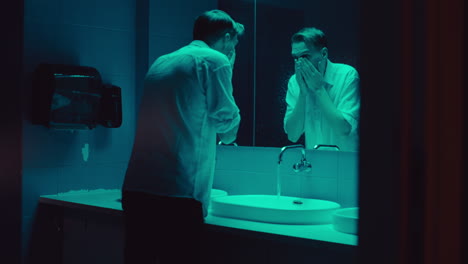 man washing face in a restroom at night