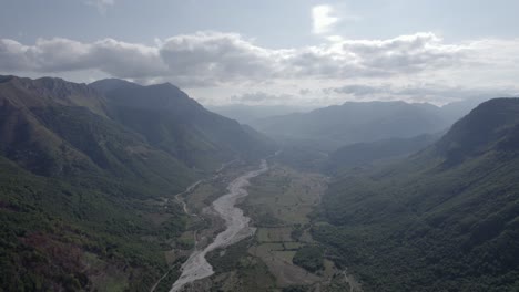 Drone-video-of-frontal-plane-advancing-over-the-Vermosh-valley-above-the-Vermoshi-river,-the-sh20-at-the-height-of-Bashkimi,-Albania,-you-can-see-small-houses-of-the-town