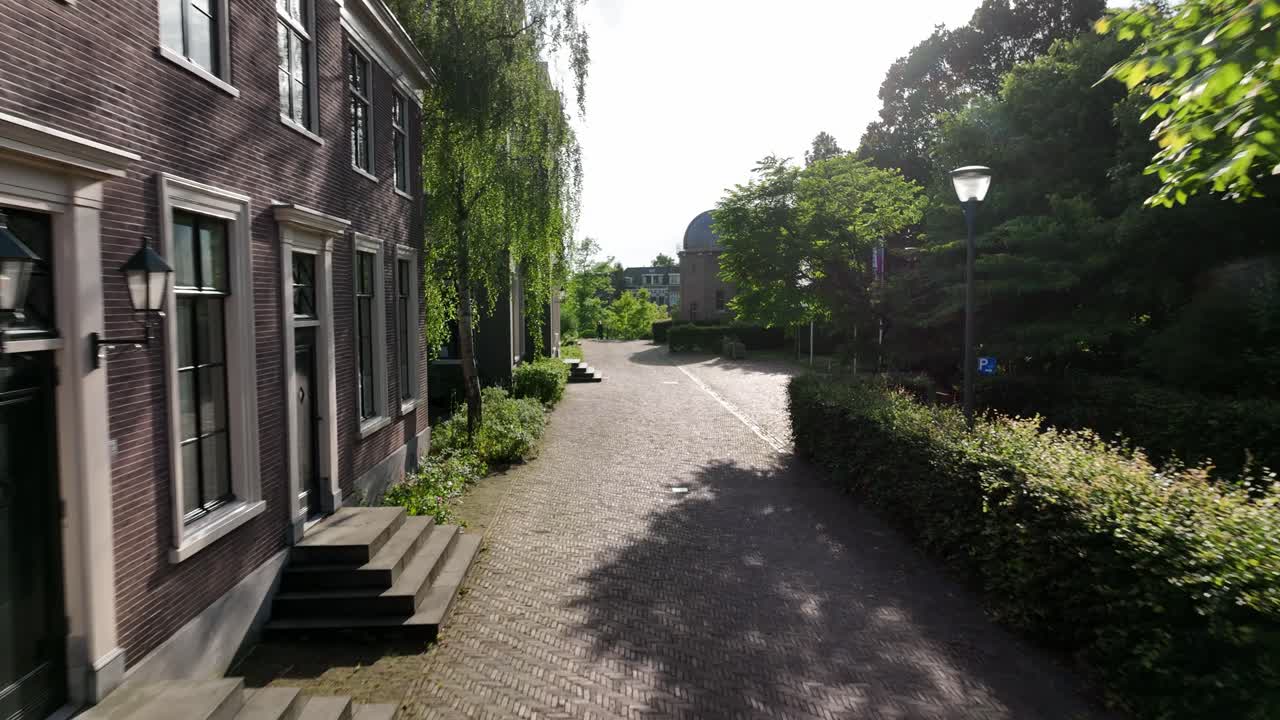 Aerial zoom in along a cobblestone street with Leiden Observatory domes visible in the background in Leiden, Netherlands